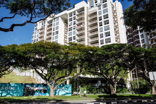 © Bloomberg. A pedestrian walks past a residential building in the Bedok area of Singapore, on Saturday, June 3, 2017. Hunger for Singapore land is adding to signs the city’s housing market is making a comeback after three years of declining prices. With new home sales surging after an easing of property restrictions in March, developers are becoming more aggressive in bidding at land auctions.