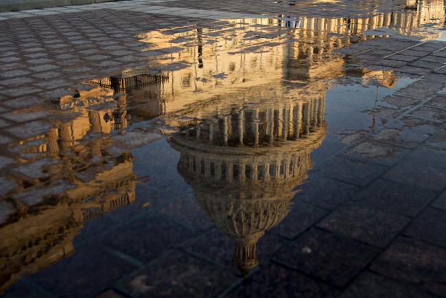© Bloomberg. The U.S. Capitol building is reflected in a puddle at sunrise in Washington, D.C., U.S.