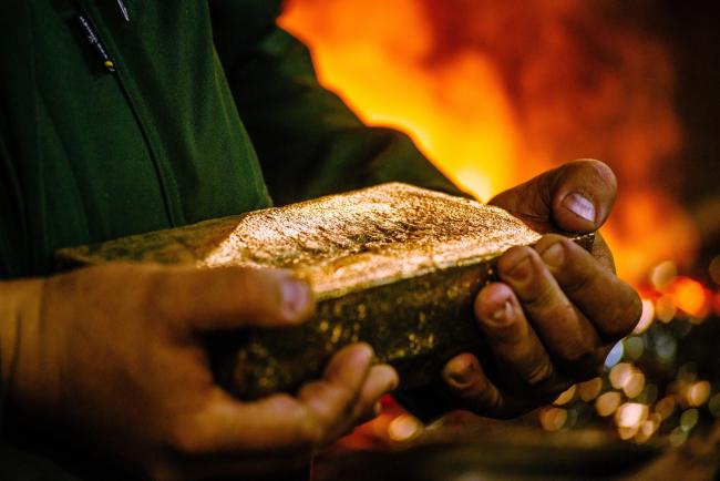 © Bloomberg. A worker carries a 28 kilogram gold bar after casting and cleaning in the foundry at the gold mine. 