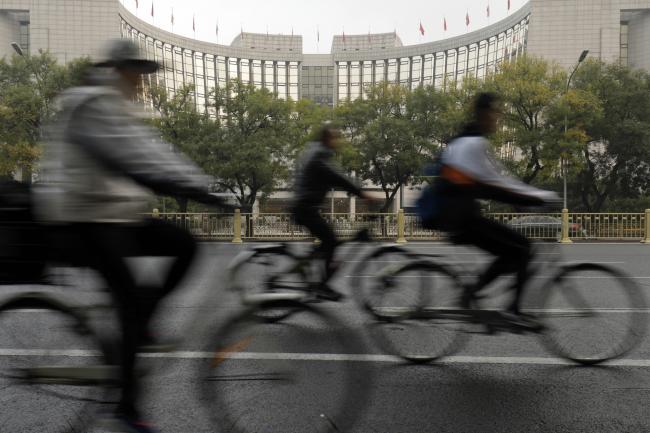 © Bloomberg. Cyclists ride past the People's Bank of China headquarters in Beijing, China, on Thursday, Oct. 19, 2017. 