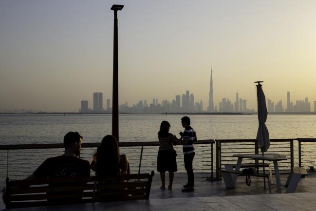 © Bloomberg. Visitors watch the sun set from the Dubai Creek Habour Development looking out towards the Burj Khalifa tower, center, and other skyscrapers in Dubai, United Arab Emirates. 
