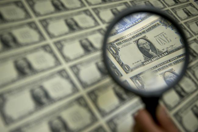 © Bloomberg. A magnifying glass is held over a 50 subject one dollar note sheet after being printed by an intaglio printing press in this arranged photograph at the U.S. Bureau of Engraving and Printing in Washington, D.C., U.S., on Tuesday, April 14, 2015. Photographer: Andrew Harrer