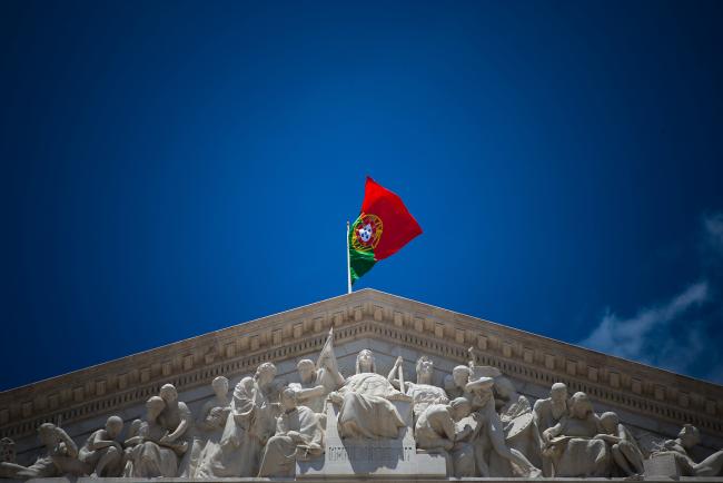 © Bloomberg. A Portuguese national flag flies above the parliament building in Lisbon, Portugal. 