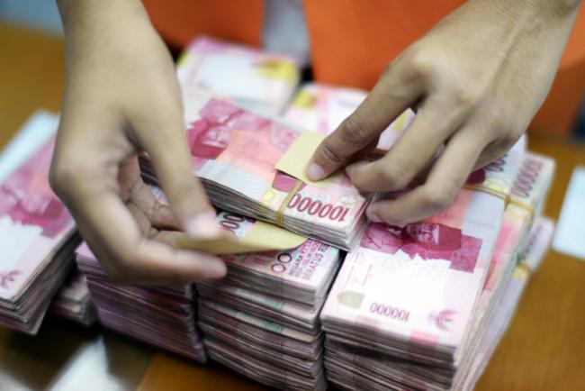 © Bloomberg. A clerk arranges bundles of Indonesian 100,000 rupiah banknotes at a currency exchange office in Jakarta, Indonesia, on Wednesday, Sept. 9, 2015.