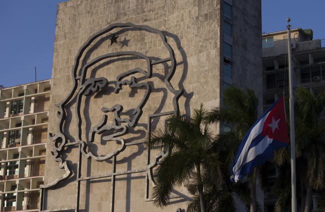 © Bloomberg. An iron sculpture of Che Guevara is displayed on the side of the Ministry of the Interior (MININT) building as a Cuban flag flies at half mast following the announcement of the death of Fidel Castro, former Cuban president, in Havana. He was 90. 