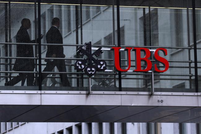 © Bloomberg. Employees pass between offices as UBS Group AG logo sits on a walkway at the UBS headquarters in Zurich, Switzerland, on Monday, Jan. 22, 2018.