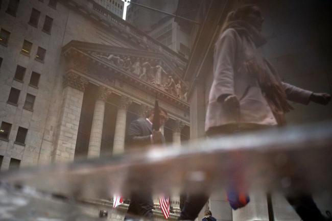 © Bloomberg. Pedestrians are reflected in a puddle while passing in front of the New York Stock Exchange (NYSE) in New York, U.S.