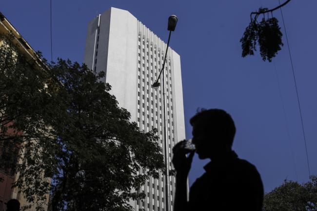 © Bloomberg. A man drinks tea as he walks past the Reserve Bank of India (RBI) headquarter building in Mumbai, India, on Friday, Jan. 27, 2017. While economists urge more investment in roads, ports and railways when the Indian government presents its budget Feb. 1, and maybe even direct cash transfers to boost consumption, a splurge carries the risk of a rating downgrade. Photographer: Dhiraj Singh/Bloomberg