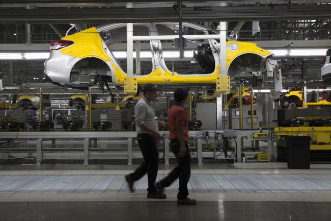 © Bloomberg. Workers walk past a vehicle frame on the production line at an ssembly plant in Pesqueria, Mexico. 