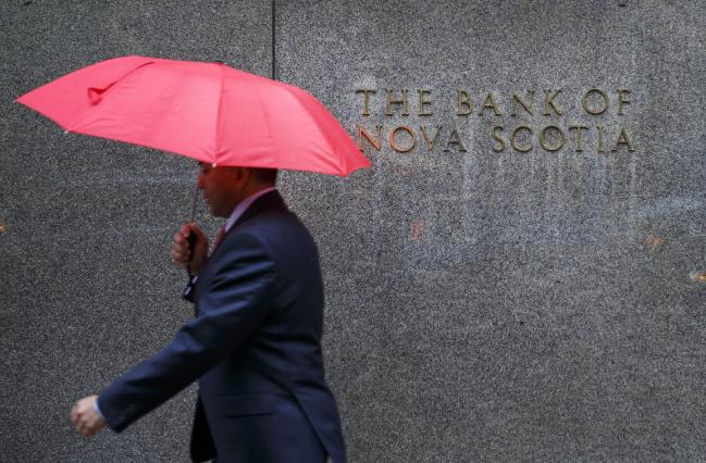 © Bloomberg. A pedestrian carrying an umbrella walks past the Bank of Nova Scotia headquarters building in Toronto, Ontario, Canada, on Tuesday, April 4, 2017. Scotiabank heads have said that the government may have to impose more measures to cool Toronto's housing market if prices remain 