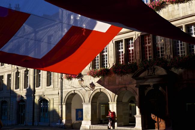© Bloomberg. A pedestrian stands beneath an awning in the colors of the Swiss national flag, outside the town hall, in Lausanne, Switzerland. Photographer: Gianluca Colla