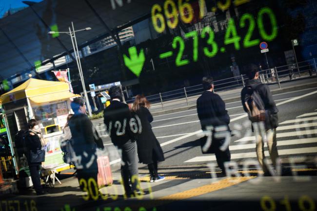 © Bloomberg. Pedestrians are reflected in an electronic stock board outside a securities firm in Tokyo, Japan, on Tuesday, Feb. 6, 2018. Japan's broad Topix index and blue-chip Nikkei 225 Stock Average were poised to enter a correction as the nation's shares headed for the biggest decline since June 2016, following U.S. peers lower amid rising concern that inflation will force interest rates higher.