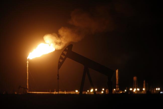 © Bloomberg. The silhouette of an electric oil pump jack is seen near a flare at night in the oil fields surrounding Midland, Texas, U.S., on Tuesday, Nov. 7, 2017.