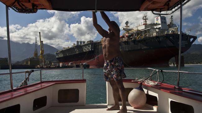 © Bloomberg. A pilot ties some knots at boat backdropped by a Petrobras oil tanker FPSO Cidade de Mangaratiba docked at Brasfels shipyard in the Jacueacanga beach, Angra dos Reis, Rio de Janeiro state , Brazil on Thursday, July 11, 2013. (Bloomberg Photo/ Dado Galdieri) 