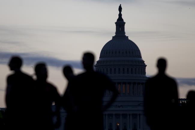 © Bloomberg. Runners wait to cross an intersection near the U.S. Capitol in Washington, D.C., U.S.