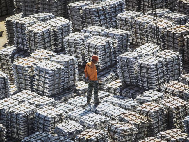 © Bloomberg. A worker stands on bundles of aluminum ingots at a China National Materials Storage and Transportation Corp. stockyard in Wuxi, China, on Thursday, Aug. 23, 2018. The U.S. and China imposed fresh tariffs on each other's goods in the middle of trade talks aimed at averting the worsening conflict between the world's two biggest economies. 