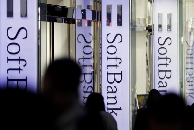 © Bloomberg. Pedestrians walk past signage for SoftBank Group Corp. outside a store in Tokyo, Japan, on Thursday, Nov. 29, 2018. SoftBank's 2.4 trillion yen ($21 billion) initial public offering of its Japanese telecommunications unit has successfully secured sales for the bulk of its shares to individual investors, people familiar with the matter said. Photographer: Kiyoshi Ota/Bloomberg