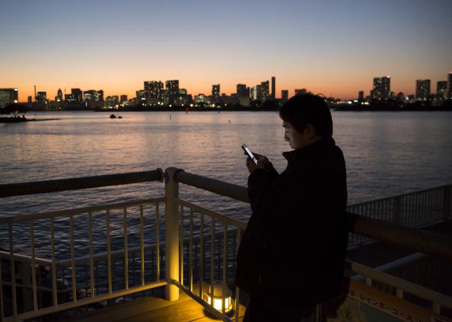 © Bloomberg. A man uses a smartphone at a pier in Tokyo, Japan, on Monday, Nov. 6, 2017. The Japanese Cabinet Office is scheduled to release third-quarter gross domestic product (GDP) data on Nov. 15, 2017.