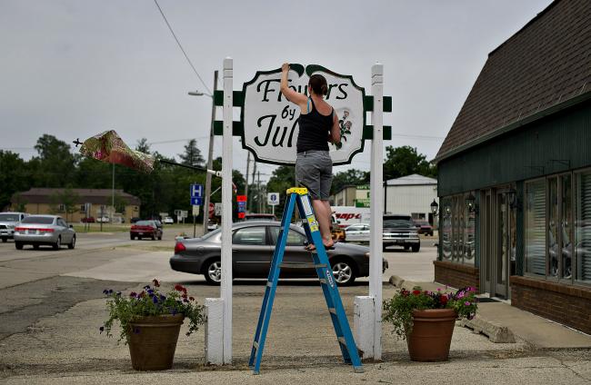 © Bloomberg. Employee Amy Merritt touches up the sign outside Flowers By Julia in Princeton, Illinois, U.S. 