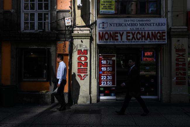 © Bloomberg. Pedestrians pass in front of a currency exchange location in Mexico City, Mexico, on Monday, Dec. 3, 2018. Mexican airport bonds rallied after the government said it will buy back a portion of debt sold to finance the now-scrapped $13 billion project, suggesting a more market-friendly approach from newly inaugurated President Andres Manuel Lopez Obrador. The Mexican Bolsa IPC index rose 1.1 percent at 42,174.03 in Mexico City. Photographer: Cesar Rodriguez/Bloomberg