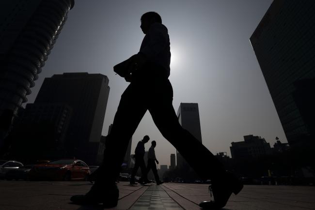 © Bloomberg. Pedestrians are silhouetted against the sun as they cross a road in Seoul, South Korea, on Thursday, Oct. 20, 2016. Long-term leave is starting to lose its stigma in South Korea, where the population spent more hours working in 2015 than all but two countries tracked by the OECD.