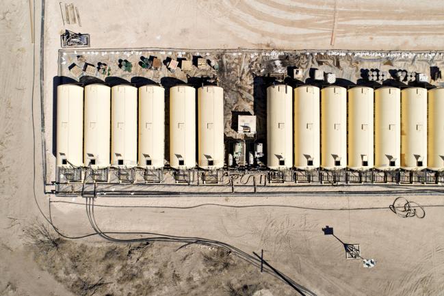 © Bloomberg. Tanks containing drilling fluid sit in a row near a Nabors Industries Ltd. rig drilling for Chevron Corp. in the Permian Basin in this aerial photograph taken near Midland, Texas, U.S.. Photographer: Daniel Acker/Bloomberg