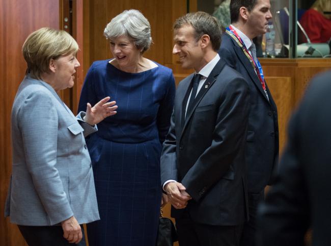 © Bloomberg. Angela Merkel, Germany's chancellor, left, speaks with Theresa May, U.K. prime minister, center, and Emmanuel Macron, France's president, ahead of roundtable talks with European Union (EU) leaders in Brussels, Belgium, on Thursday, Oct. 19, 2017. May will demand that the European Union move Brexit talks on to trade in a face-to-face showdown with leaders over dinner, even as EU officials see a breakthrough as all but impossible.