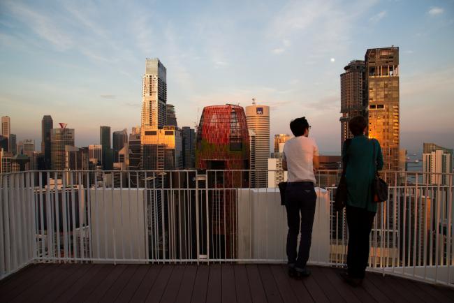 © Bloomberg. Visitors look out at the skyline from the skybridge at the Pinnacle@Duxton, a Housing & Development Board (HDB) public housing estate, in Singapore, on Thursday, Sept. 15, 2016. Singapore is currently mired in its most prolonged housing slump on record. Home prices in the city-state fell for the 11th straight quarter in the three months ending June 30, posting the longest losing streak since records started in 1975. 