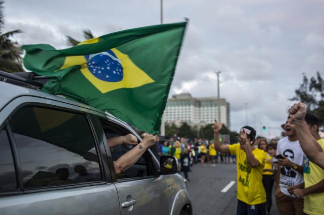 © Bloomberg. Supporters of Jair Bolsonaro, presidential candidate for the Social Liberal Party (PSL), wave a Brazilian national flag from a car while celebrating after polls closed during the second round of presidential elections in Rio de Janeiro, Brazil, on Sunday, Oct. 28, 2018. Bolsonaro swept to power in Brazil's presidential election Sunday, marking a hard pivot to the right that promises to open up the resource-rich economy to private investment, strengthen ties to the U.S. and unleash an aggressive crackdown on epidemic crime. 