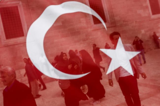 © Bloomberg. People stand behind a Turkish national flag after attending Friday prayers at the Fatih Mosque in Istanbul, Turkey. Photographer: Kostas Tsironis/Bloomberg