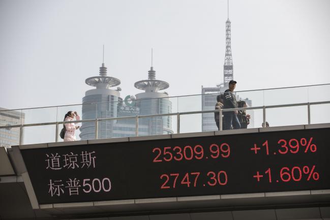 © Bloomberg. People walk along an elevated walkway as an electronic ticker displays the figures of the Dow Jones Industrial Average, top, and the Standard & Poor's 500 Index in the Lujiazui Financial District in Shanghai, China, on Monday, Feb. 26, 2018. Xi Jinping's decision to cast aside China's presidential term limits is stoking concern he also intends to shun international rules on trade and finance, even as he champions them on the world stage. 
