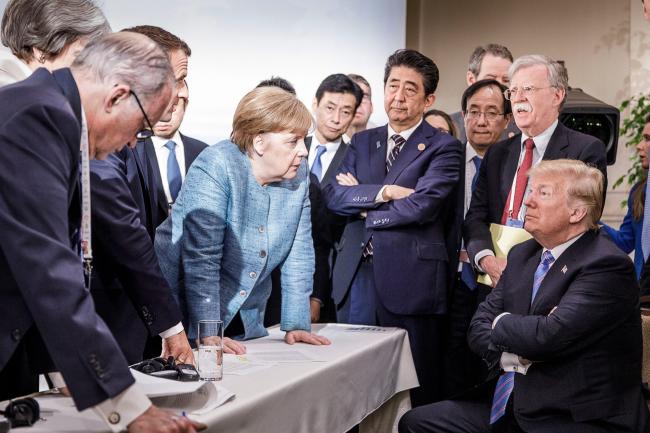 © Bloomberg. Angela Merkel , German Chancellor, deliberates with US president Donald Trump on the sidelines of the official agenda on the second day of the G7 summit on June 9, 2018 in Charlevoix, Canada. Also pictured are (L-R) Larry Kudlow, director of the US National Economic Council, Theresa May, UK prime minister, Emmanuel Macron, French president, Angela Merkel, Yasutoshi Nishimura, Japanese deputy chief cabinet secretary, Shinzo Abe, Japan prime minister, Kazuyuki Yamazaki, Japanese senior deputy minister for foreign affairs, John Bolton, US national security adviser, and Donald Trump. Canada are hosting the leaders of the UK, Italy, the US, France, Germany and Japan for the two day summit. 