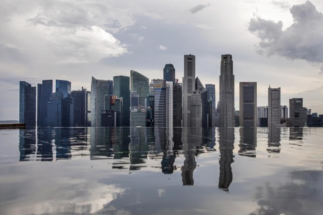 © Bloomberg. Commercial buildings standing in the central business district are reflected in a rooftop pool in Singapore, on Wednesday, June 13, 2018. Tourism as well as the consumer sector will likely see a lift thanks to the influx of international media at the recent DPRK-USA Summit, according to RHB Research Institute Singapore Pte. Photographer: Brent Lewin/Bloomberg