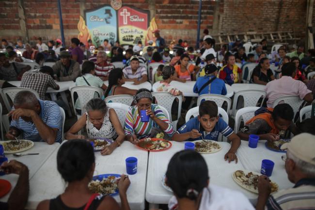 © Bloomberg. People eat at a soup kitchen during a meal service for Venezuelan migrants in the town of La Parada, Cucuta, Colombia, on Feb. 11. Photographer: Ivan Valencia/Bloomberg