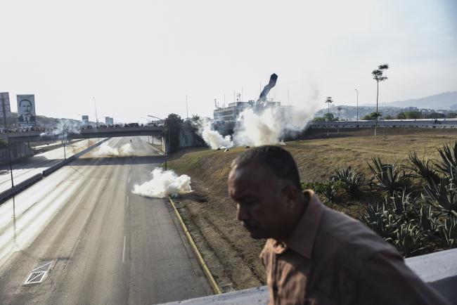 © Bloomberg. A man runs from tear gas on the Francisco Fajardo Highway during a military uprising in Caracas on April 30. Photographer: Carlos Becerra/Bloomberg