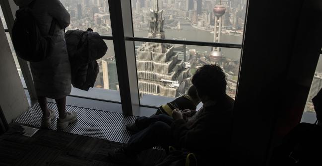 © Bloomberg. People look at the view from the observation deck at the Shanghai World Financial Center as the Jin Mao Tower, center, and the Oriental Pearl Tower, right, stand in Shanghai.