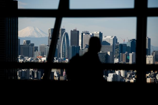 © Bloomberg. Mount Fuji stands beyond buildings as a visitor looks out at the skyline from an observation deck in Tokyo, Japan, on Friday, Jan. 11, 2019. Japan’s key inflation gauge slowed in the first back-to-back decline since April, highlighting the difficulty of the Bank of Japan’s price goal ahead of its policy meeting next week. Photographer: Akio Kon/Bloomberg