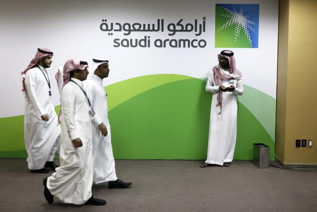 © Bloomberg. Attendees walk by a sign for the Saudi Arabian Oil Co. (Aramco) on display inside the King Abdulaziz Center for World Culture during a tour of the project in Dhahran, Saudi Arabia, on Friday, Nov. 25, 2016.