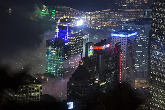 © Bloomberg. The Standard Chartered Bank building, center, HSBC Holdings Plc headquarters building, center right, and other buildings standing illuminated and shrouded in clouds are seen from Victoria Peak at night in Hong Kong, China, on Wednesday, April 6, 2016.  Photographer: Justin Chin/Bloomberg