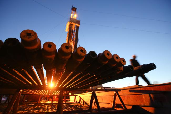 © Bloomberg. A worker passes an illuminated oil drilling rig and drill pipes, operated by Rosneft PJSC, in the Samotlor oilfield near Nizhnevartovsk, Russia, on Tuesday, March 21, 2017. 