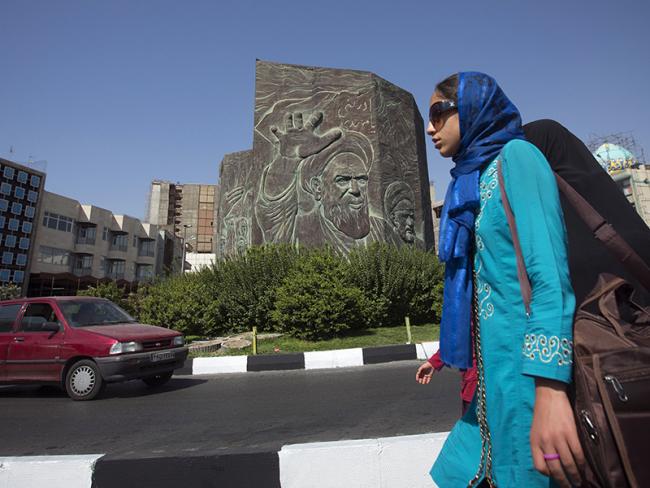 © Bloomberg. Pedestrians pass a public monument showing the face of Ruhollah Khomeini, founder of the Islamic republic of Iran, in Tehran, Iran. 