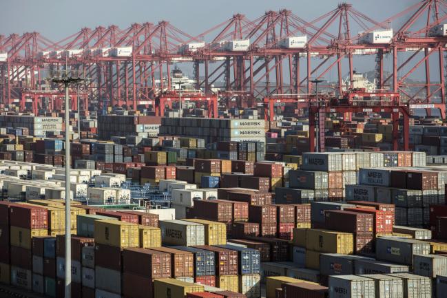 © Bloomberg. Containers sit stacked next to gantry cranes at the Yangshan Deep Water Port in Shanghai, China, on Tuesday, July 10, 2018. China told companies to boost imports of goods from soybeans to seafood and automobiles from countries other than the U.S. after trade tensions between the world's two biggest economies escalated into a tariff war last week. 