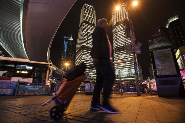 © Bloomberg. A man pulling a shopping trolley walks past commercial buildings standing illuminated at night in the Lujiazui Financial District in Shanghai, China, on Friday, Oct. 13, 2017. A number of economic indicators show 