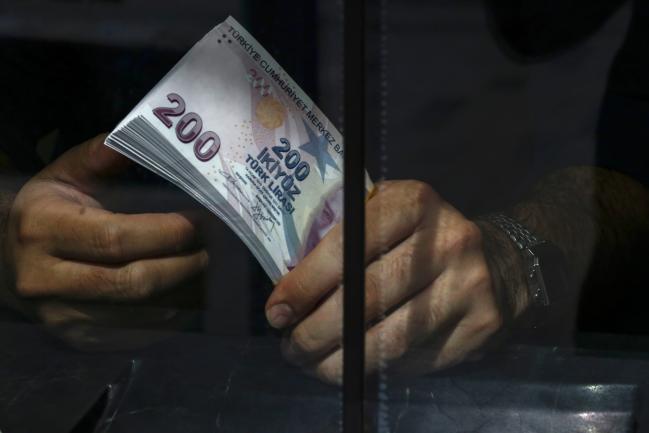 © Bloomberg. An emloyee holds a wad of 200 Turkish lira banknotes in a currency exchange in Istanbul, Turkey. Photographer: Kostas Tsironis/Bloomberg