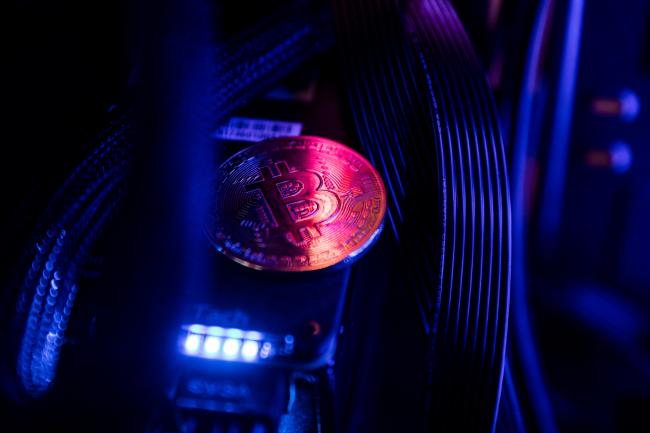 © Bloomberg. A token representing Bitcoin virtual currency sits among cables and LED lighting inside a 'mining rig' computer in this arranged photograph in Budapest, Hungary. 