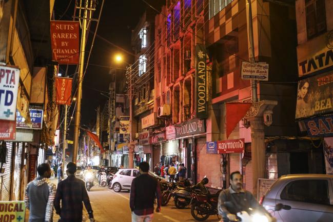 © Bloomberg. Motorcyclists ride past pedestrians walking in Raghunath Market at night in Jammu, Jammu and Kashmir, India, on Wednesday, Nov. 15, 2017. The head of treasury at State Bank of India is betting against the street. Inflation will stay anchored after the recent uptick, giving the central bank room to cut interest rates and bonds to rally, C. Venkat Nageswar said. 