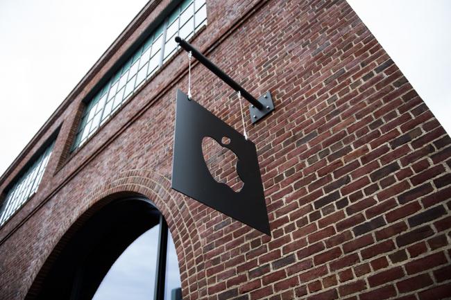 © Bloomberg. Apple Inc. signage hangs outside of the company's Williamsburg store in the Brooklyn borough of New York, U.S., on Friday, May 20, 2017. Apple Chief Executive Officer Tim Cook said in May that the company planned to invest at least $1 billion to back advanced manufacturing companies in the U.S. and help create jobs in the industry. Photographer: Mark Kauzlarich/Bloomberg