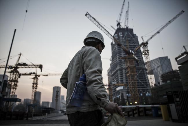 © Bloomberg. A worker walks past cranes operating on a construction site in Beijing, China. Photographer: Qilai Shen