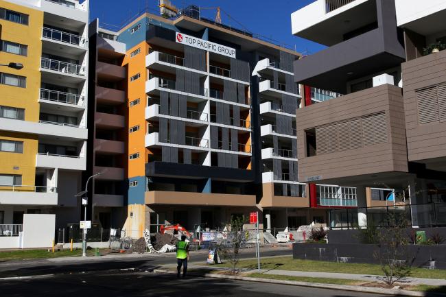 © Bloomberg. A security guard walks towards a residential construction site in the suburb of Wolli Creek in Sydney, Australia, on Sunday, June 17, 2018. Australia is riding out a huge gamble on property. The bet: 27 years of recession-free economic growth—during which Sydney home prices surged fivefold—would continue unabated and allow borrowers to keep servicing their debt. Photographer: Lisa Maree Williams/Bloomberg