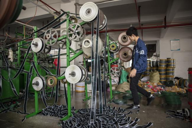 © Bloomberg. An employee walks as polyvinyl chloride (PVC) are fed into machines to make artificial Christmas tree branches on the production line at the Bosen Gongyi Co. factory in Yiwu, Zhejiang province, China, on Thursday, Oct. 25, 2018. U.S. President Donald Trump's trade war was supposed to be the Grinch to steal the Christmas cheer from this holiday-exporting hub about 175 miles southwest of Shanghai. But, so far at least, it looks as if the enduring power of globalization—and entrenched supply chains—is winning out. Photographer: Qilai Shen/Bloomberg